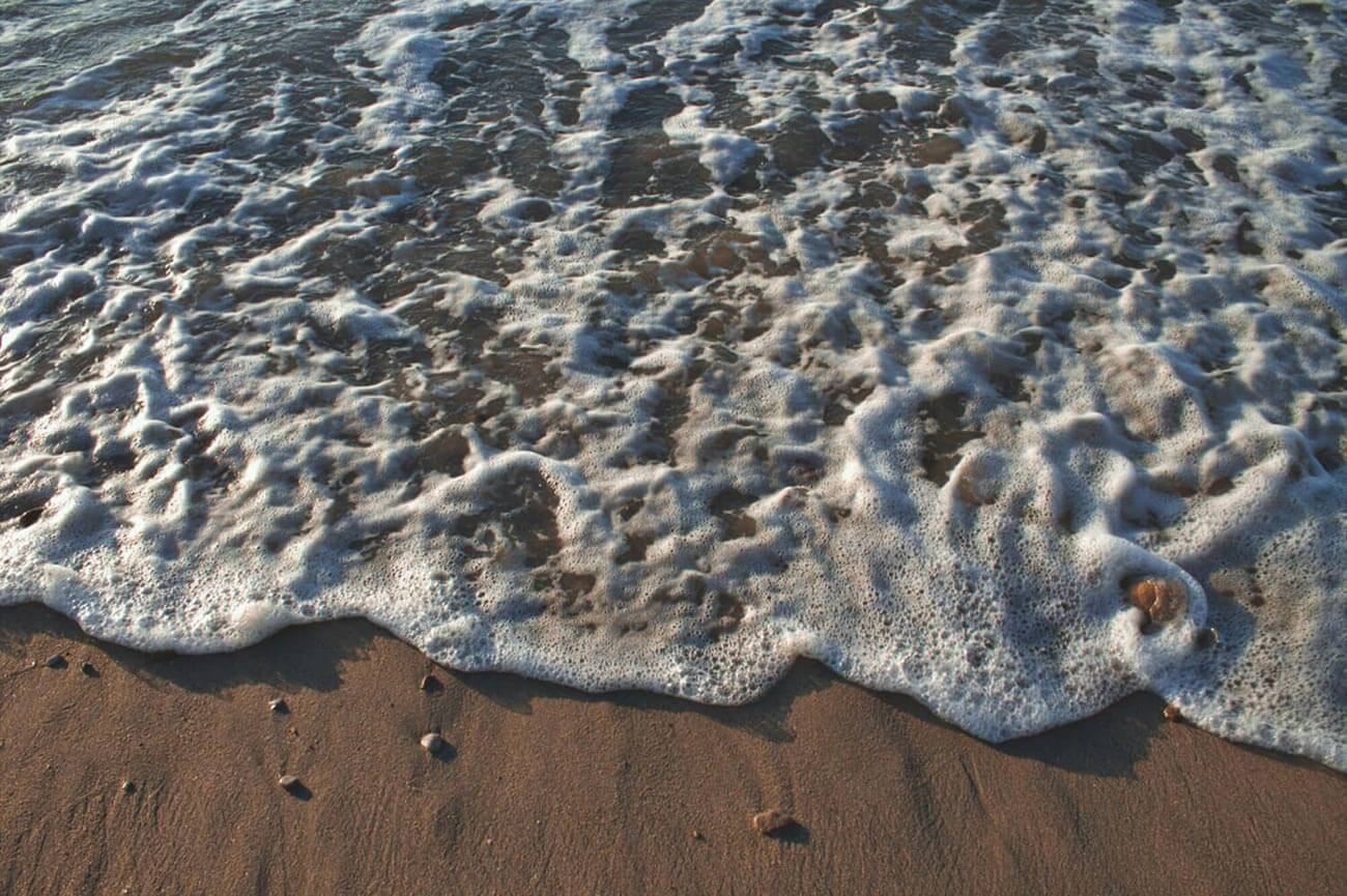 Nahaufnahme von Meeresschaum, der an Strand spült