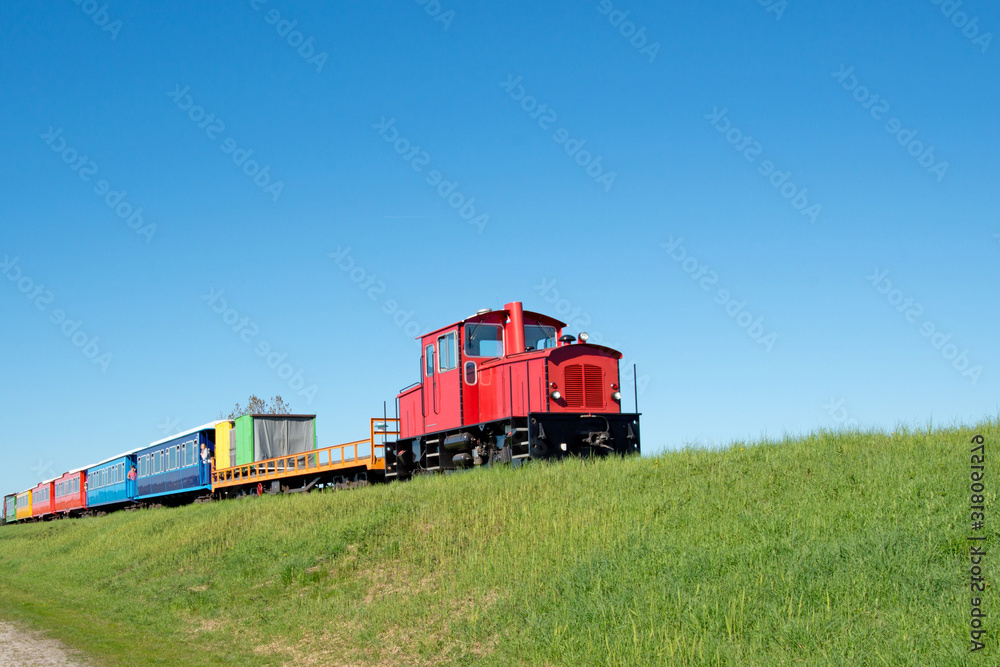 kleine Inselbahn mit bunten Wagons fährt über einen Hügel