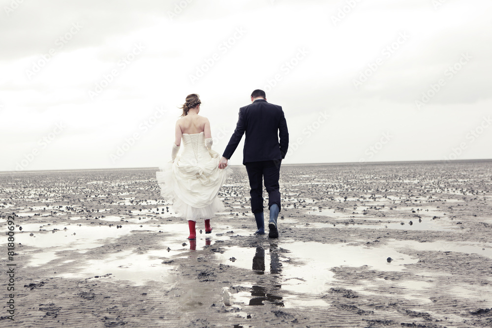 Brautpaar in Gummistiefeln spaziert durch das Wattmeer